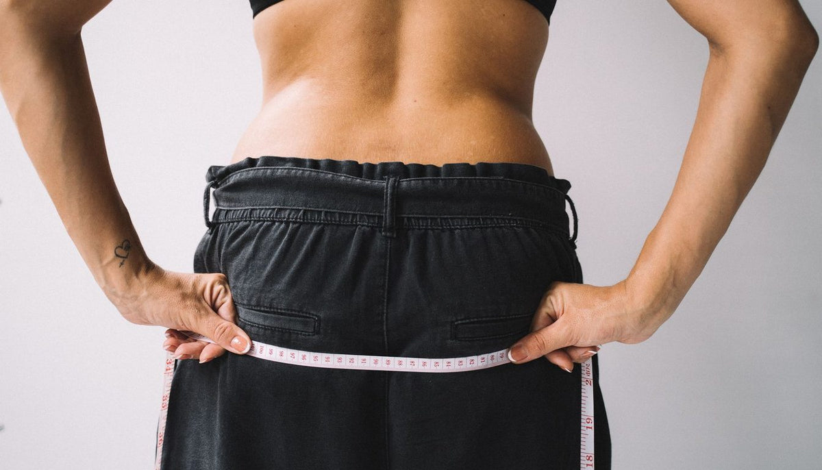 Prise de mesure du tour de taille au mètre ruban, sur un pantalon foncé